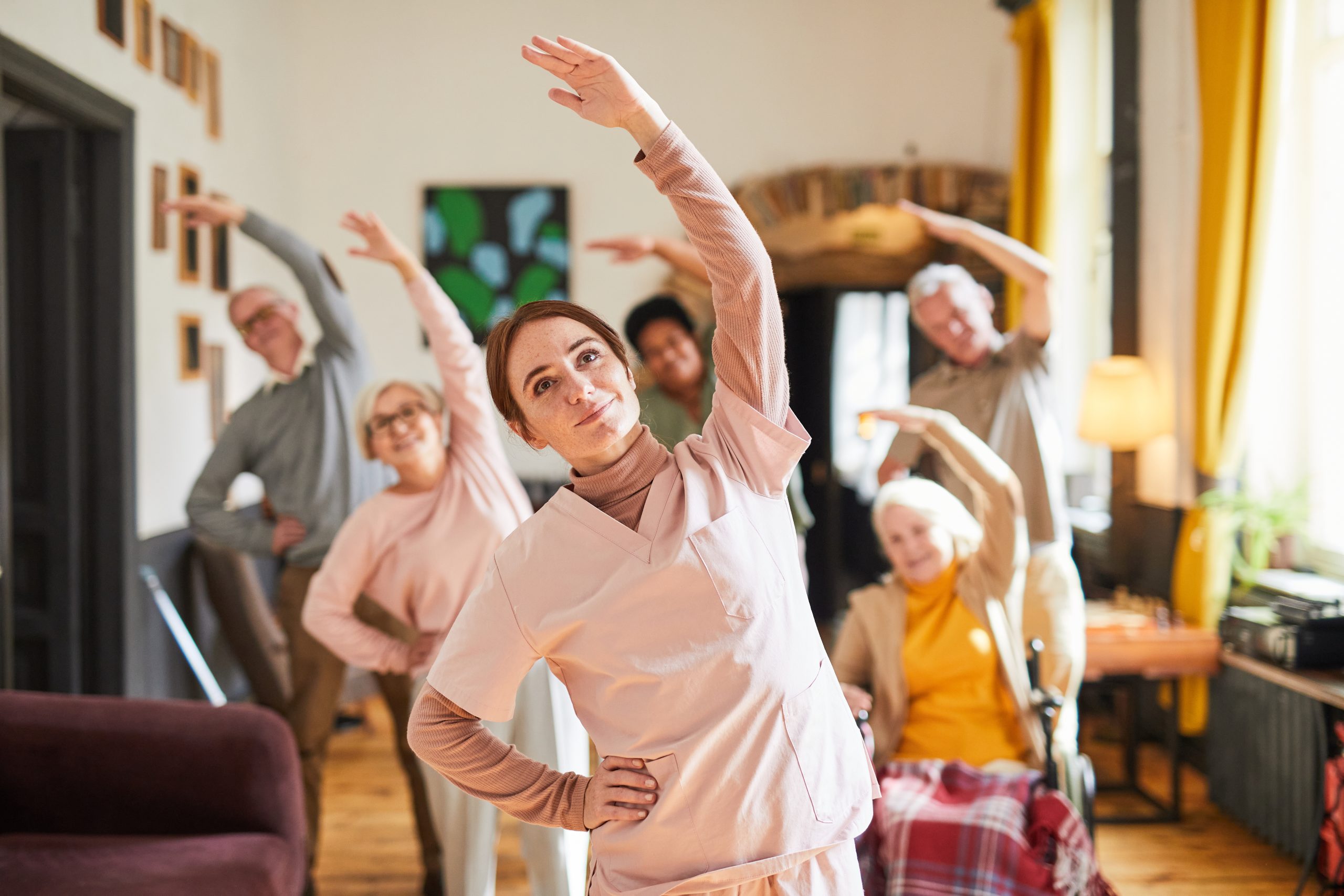 Waist up portrait young woman coordinating group of senior people enjoying morning exercises in retirement home